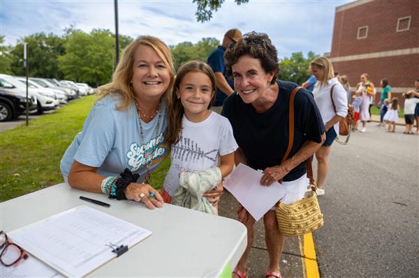 mom, student and teacher smiling near a table